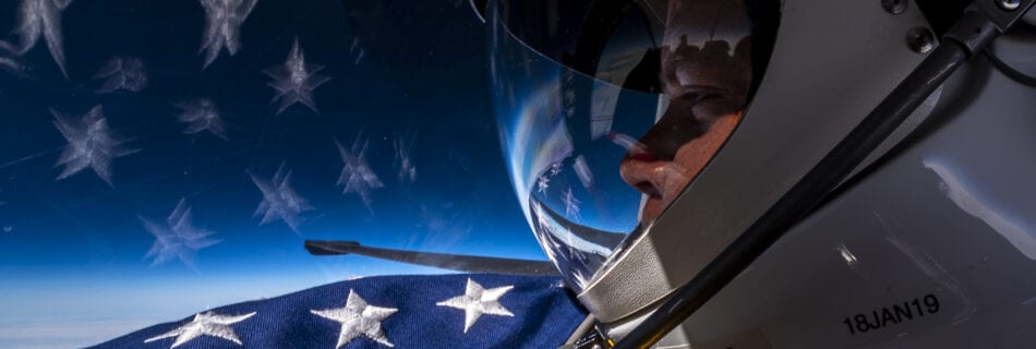 Extreme Ross stares over the stars from a flag out past the wing of a U-2